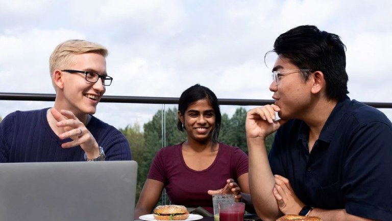 Three students discussing outdoors in front of a laptop
