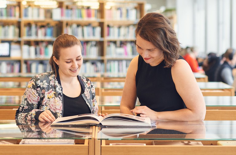 Two women reading a book at a library