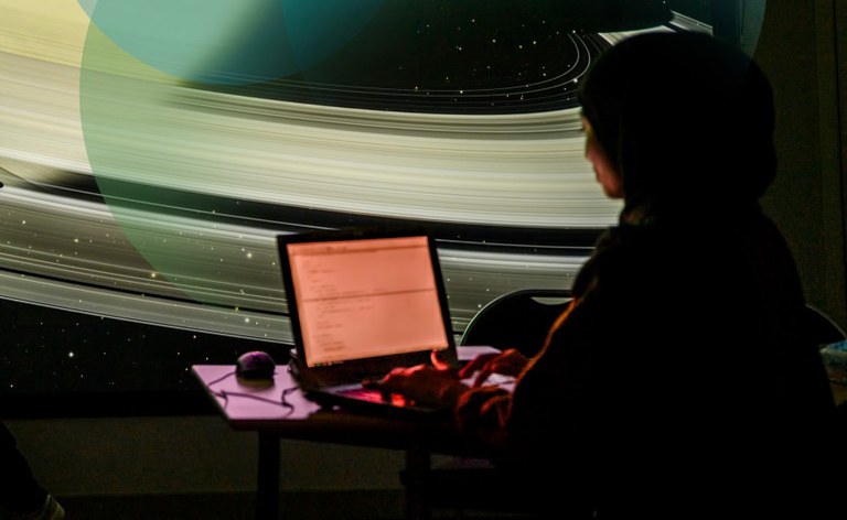 Woman working on a laptop in front of a outter space projection.