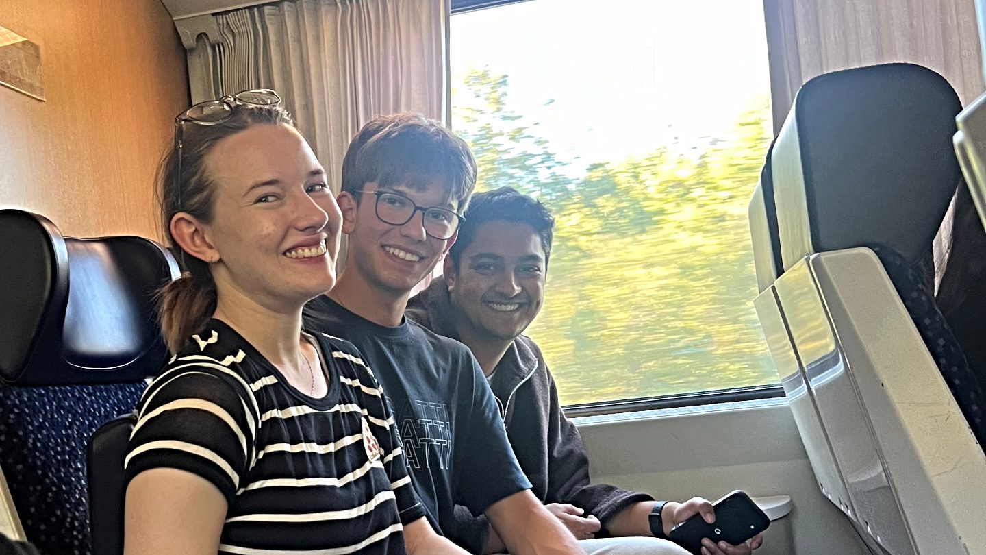 Three students on a train smiling at the camera
