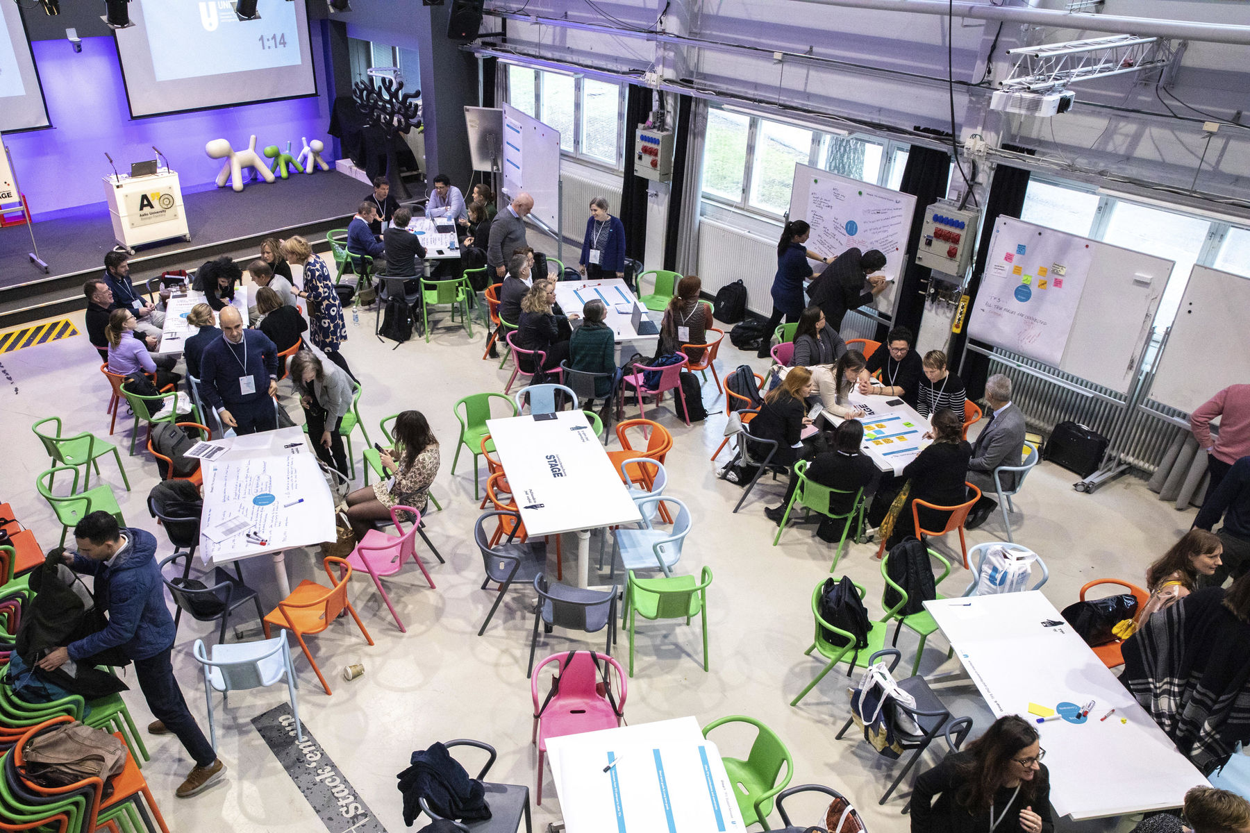 Photograph of a meeting full of grups of people sitting on tables discussing