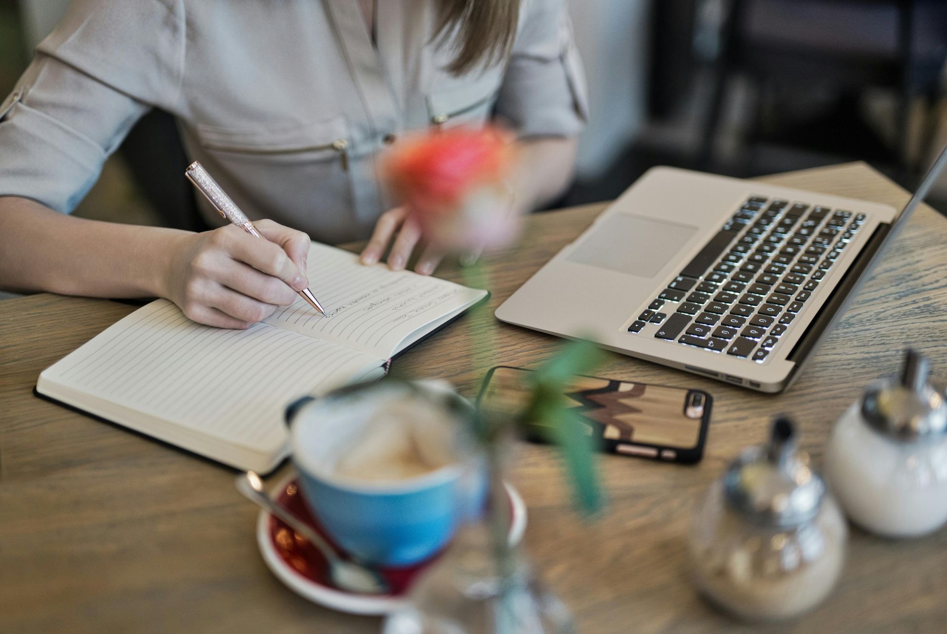 A person writing in a notebook, with a coffee and a laptop nearby